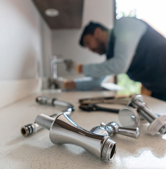 A man fixing a faucet in the kitchen with bunch of tools around him.